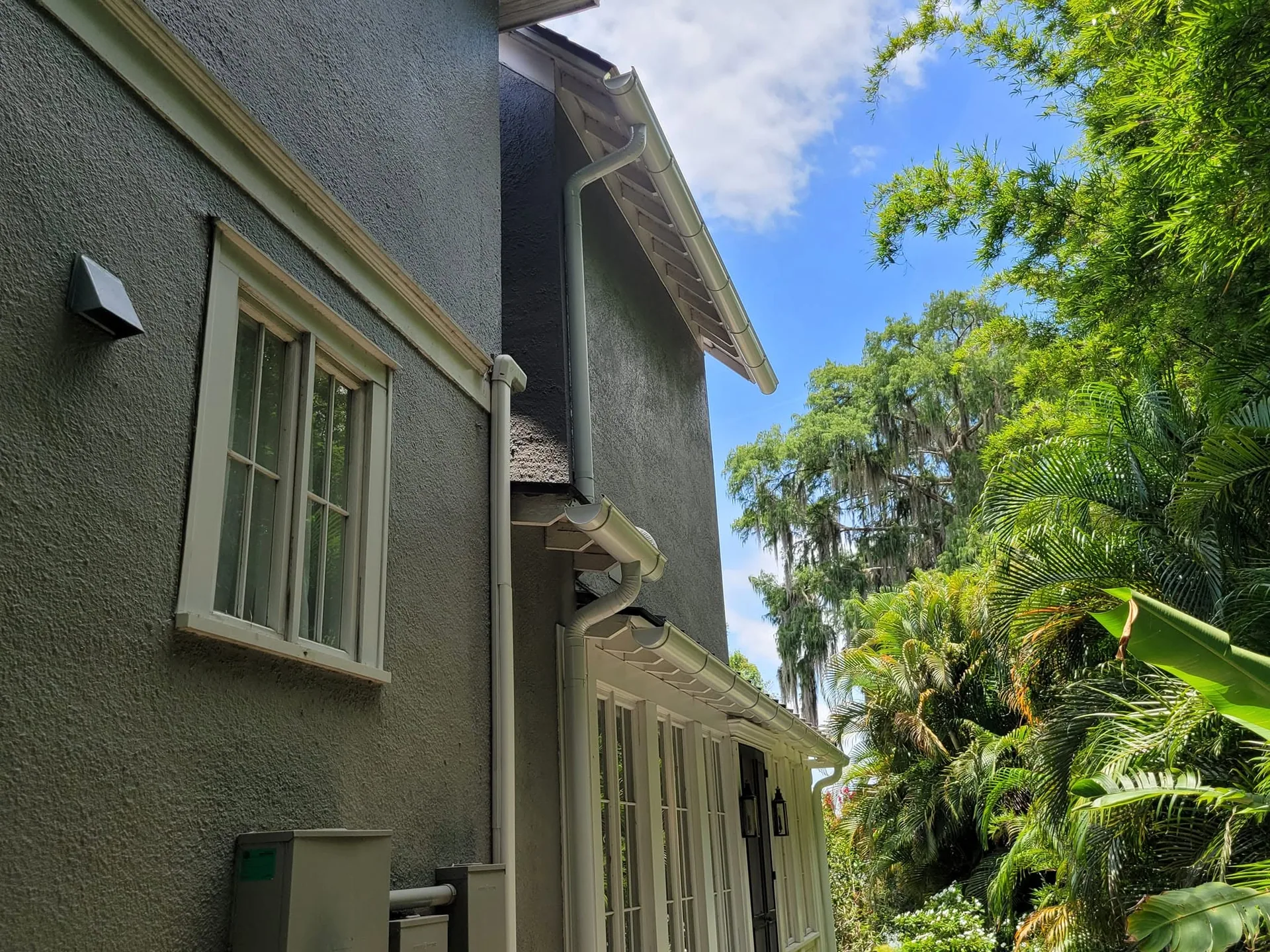 Low angle white round downspout dark gray stucco two story side wall tropical la